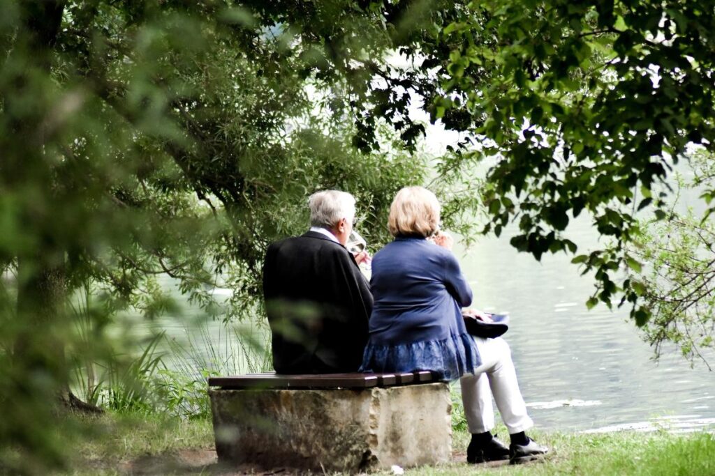 a man and woman sitting on a bench by a lake